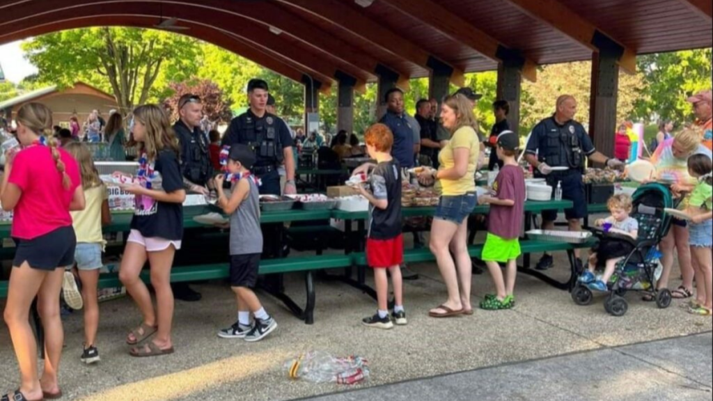 A picture of police standing behind a long picnic table serving food to members of the community.