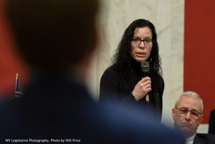 A woman with dark hair and wearing glasses speaks into a microphone on the West Virginia Senate floor.