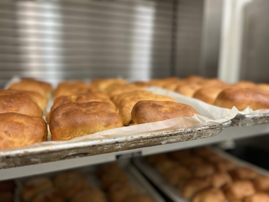 Dozens of fresh pepperoni rolls are shown on baking sheets. They are a golden brown in color.