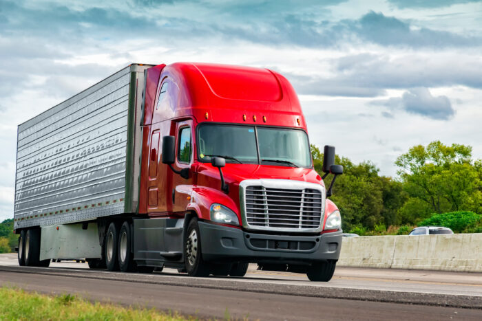 Horizontal shot of a red semi-truck on an interstate highway.