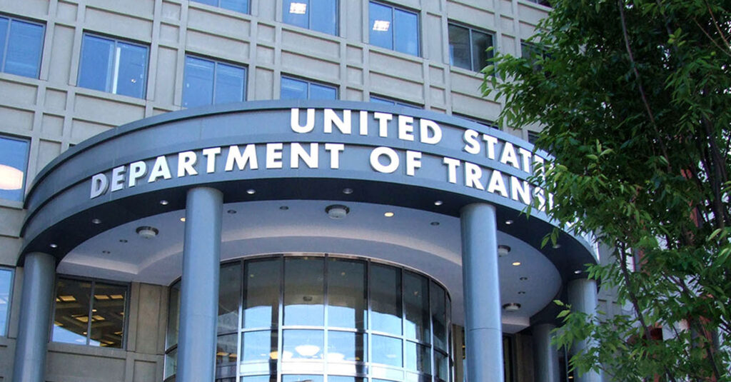A federal building with a curved entrance and glass windows and a tree is the headquarters of USDOT.