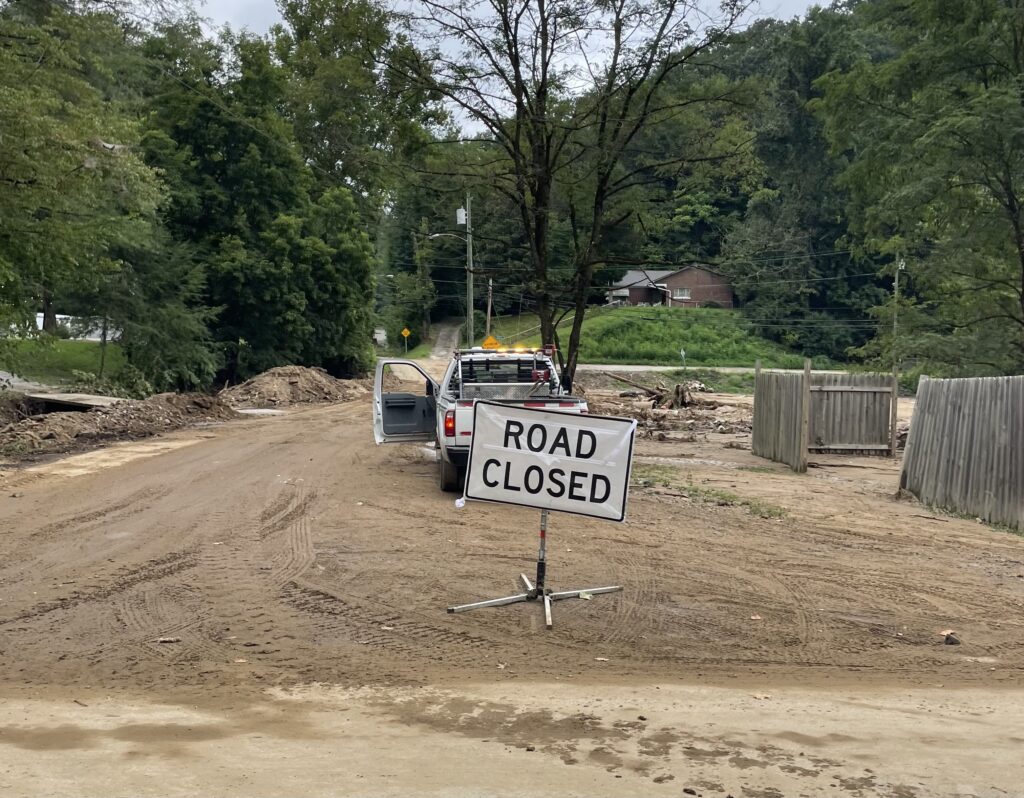 A road covered in dirt and tread marks has a sign in front of it that says road closed.