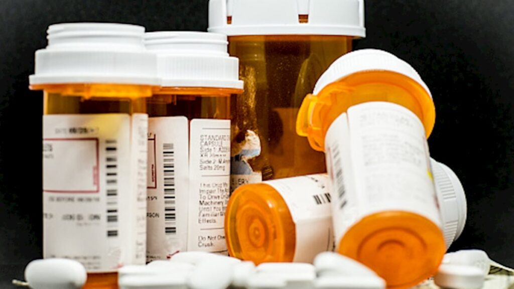 A row of pill bottles is seen laying on top of prescription medication.