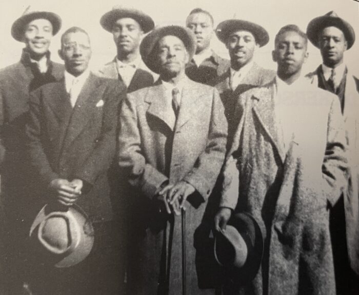 A black and white photo. Eight men stand next to each other and are formally dressed.