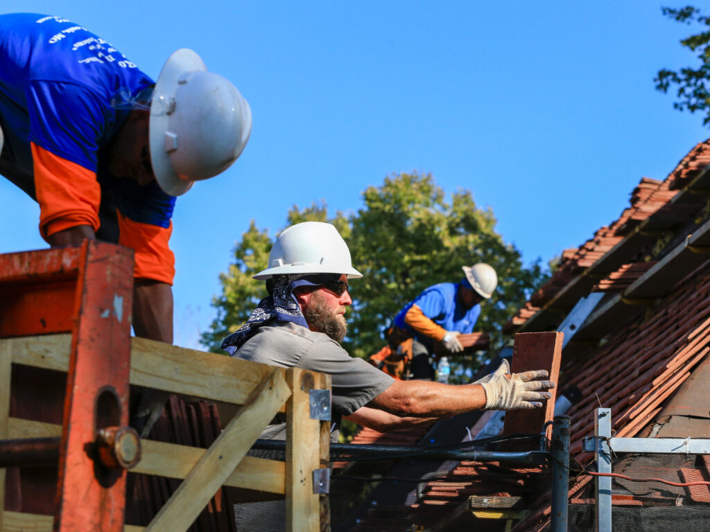 Construction workers are seen replacing red roof tiles.