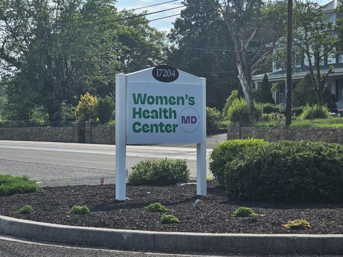 A white sign with green lettering signals the parking lot for the Women's Health Center of Maryland.