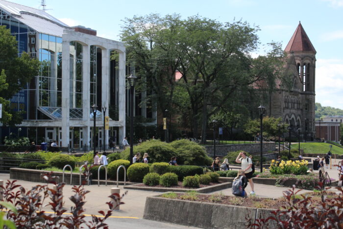 A building with white pillars is seen in the background with green gardens in the foreground.