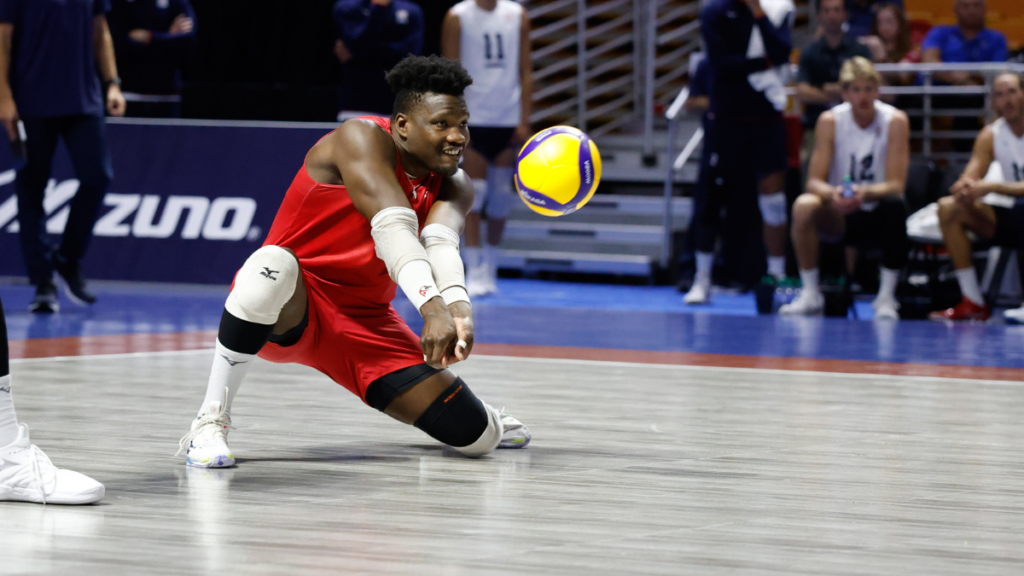 A man crouched down on a volleyball court hitting a ball