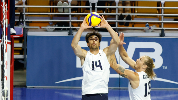A man in a white uniform shirt and black shorts holds a volleyball