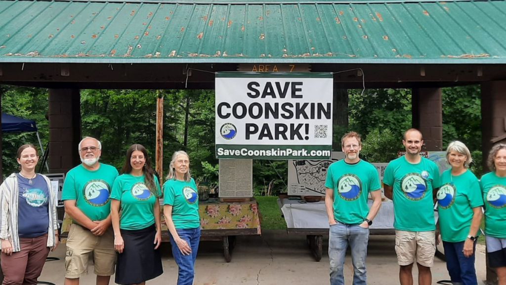 A group of people in green shirts stand in front of a park shelter