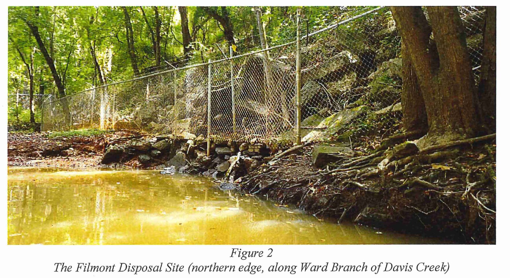 Discolored creek water with a chain link fence