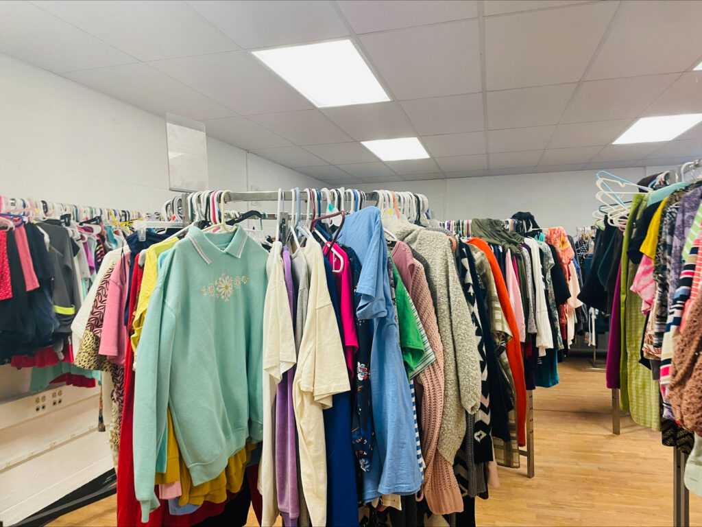 Colorful clothes on circular clothing racks sit in the middle of the room.