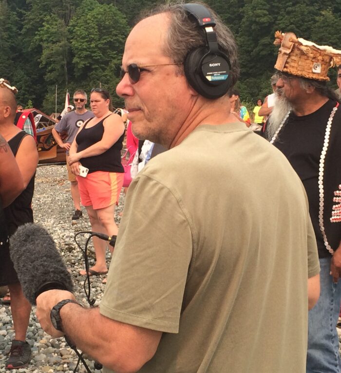 A photo of Howard Berkes from the field. He holds a shotgun mic and wears over the ears headphones.