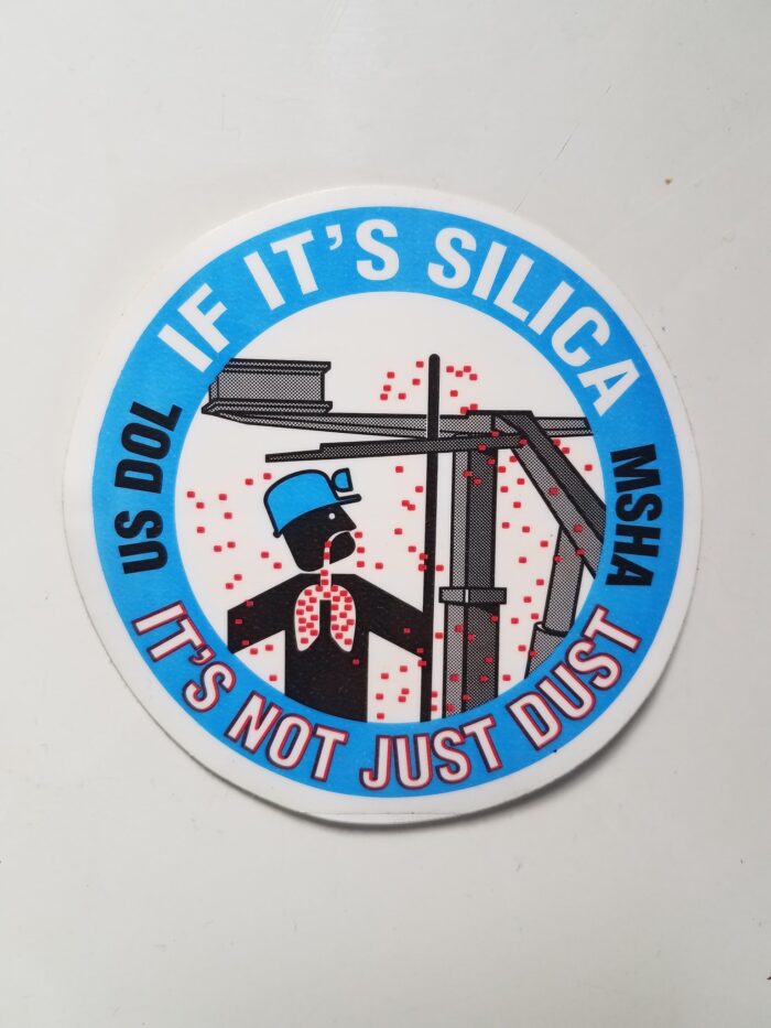A sticker is seen that reads "If it's Silica, It's Not Just Dust." The image on the sticker shows a cartoon coal miner breathing in red dust.