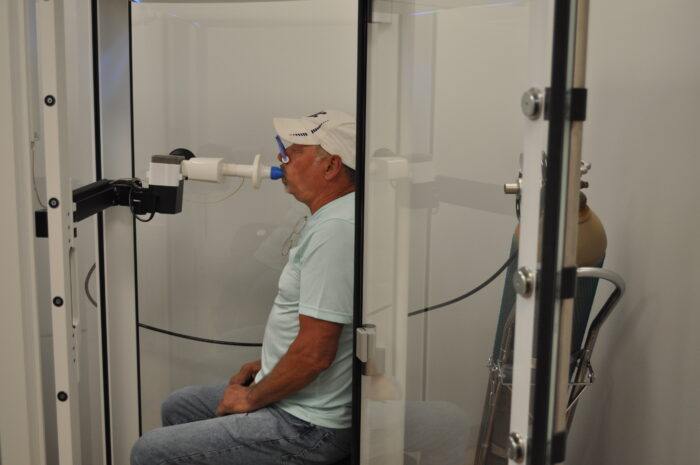 A coal miner sits in a booth and takes a breathing test.