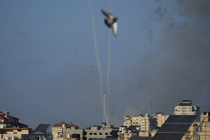 Pigeon flies by the camera as missiles rain on a middle eastern city.