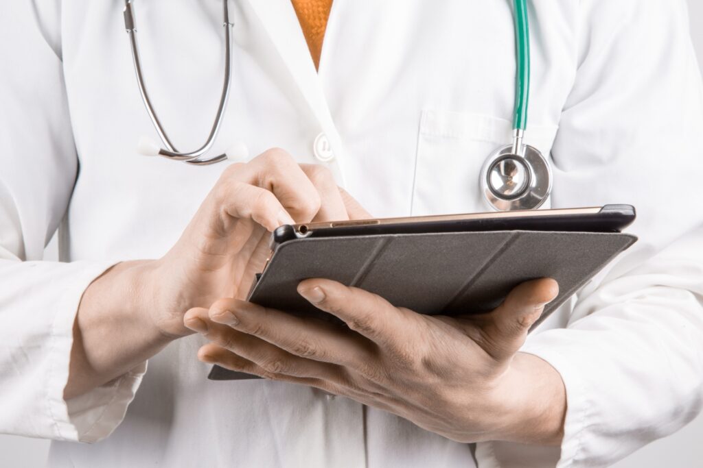 A doctor wearing a white lab coat and stethoscope reports patient data on an iPad.