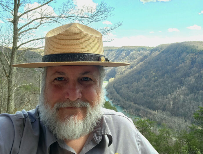 A man with a white beard and park ranger hat takes a selfie. 