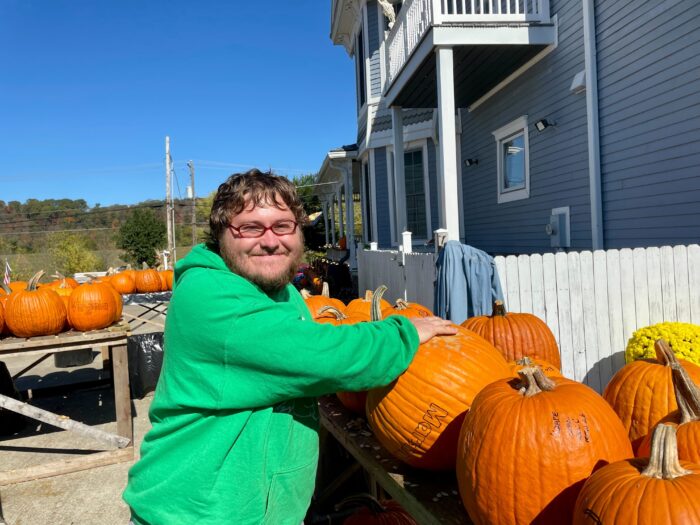 Man in green hoodie poses for a phot while cleaning out pumpkins.
