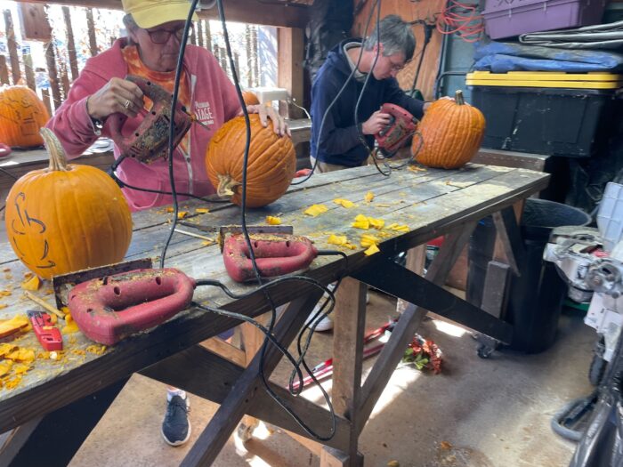 Two people saw the pumpkins at a table in a shed.
