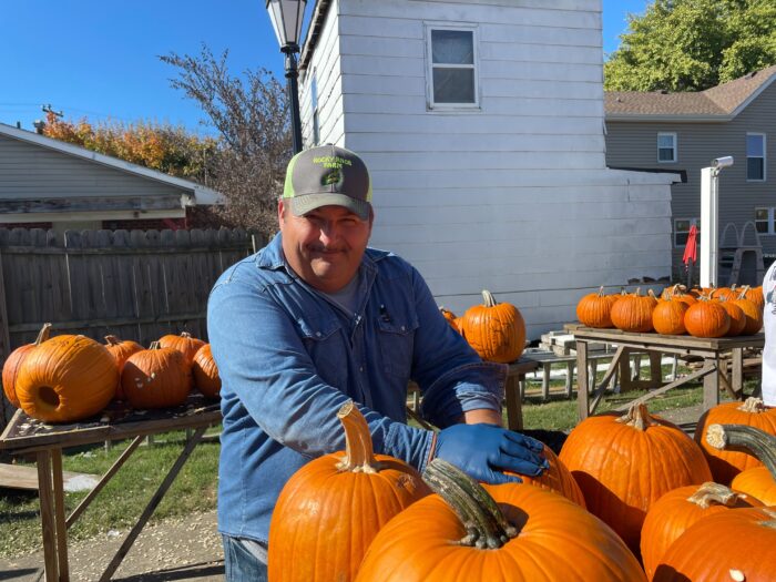 Man with hat on looks into the caption while cleaning out a pumpkin.