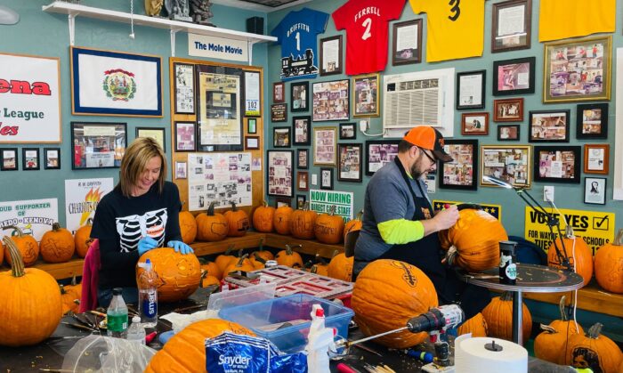 A man and a woman carve pumpkins in a garage.