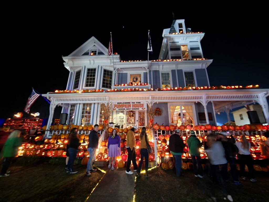 Upshot of large blue Victorian style home with hundreds of pumpkins around it.