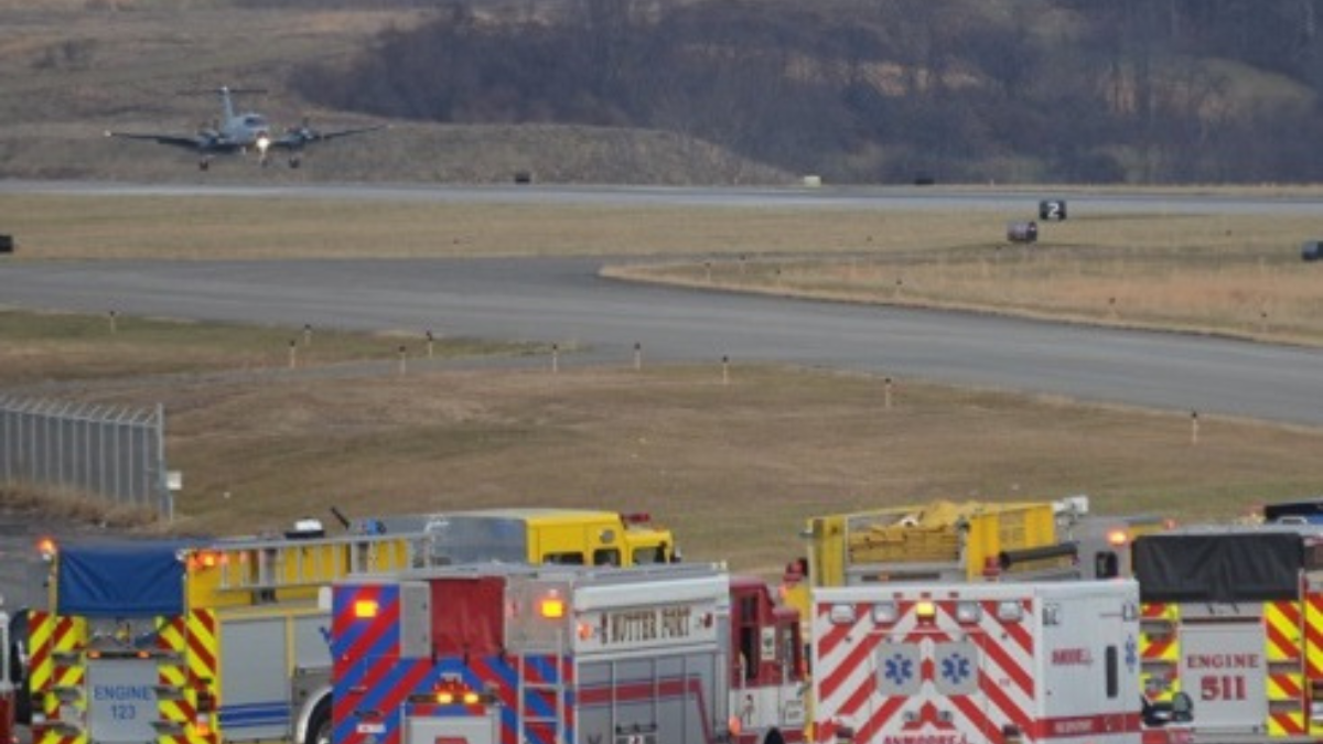Emergency vehicles surround an airport runway with a plane landing in the background