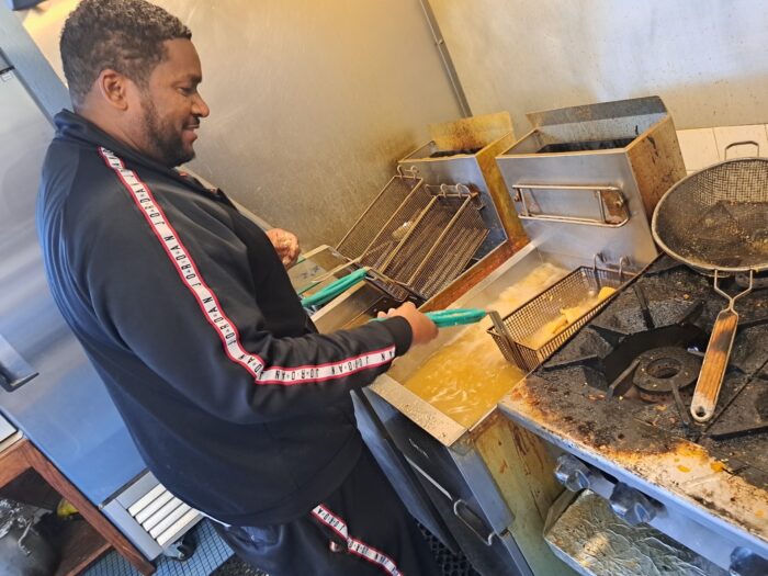 A man in a black jacket stands over a fryer frying fish.