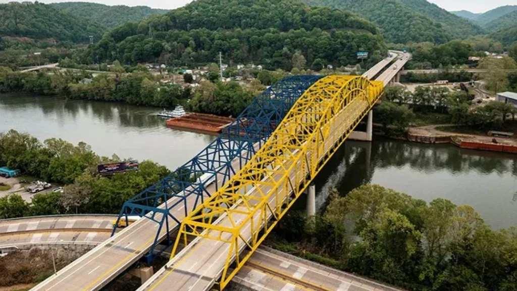 A gold and blue painted bridge crosses a river with green mountains in the background.