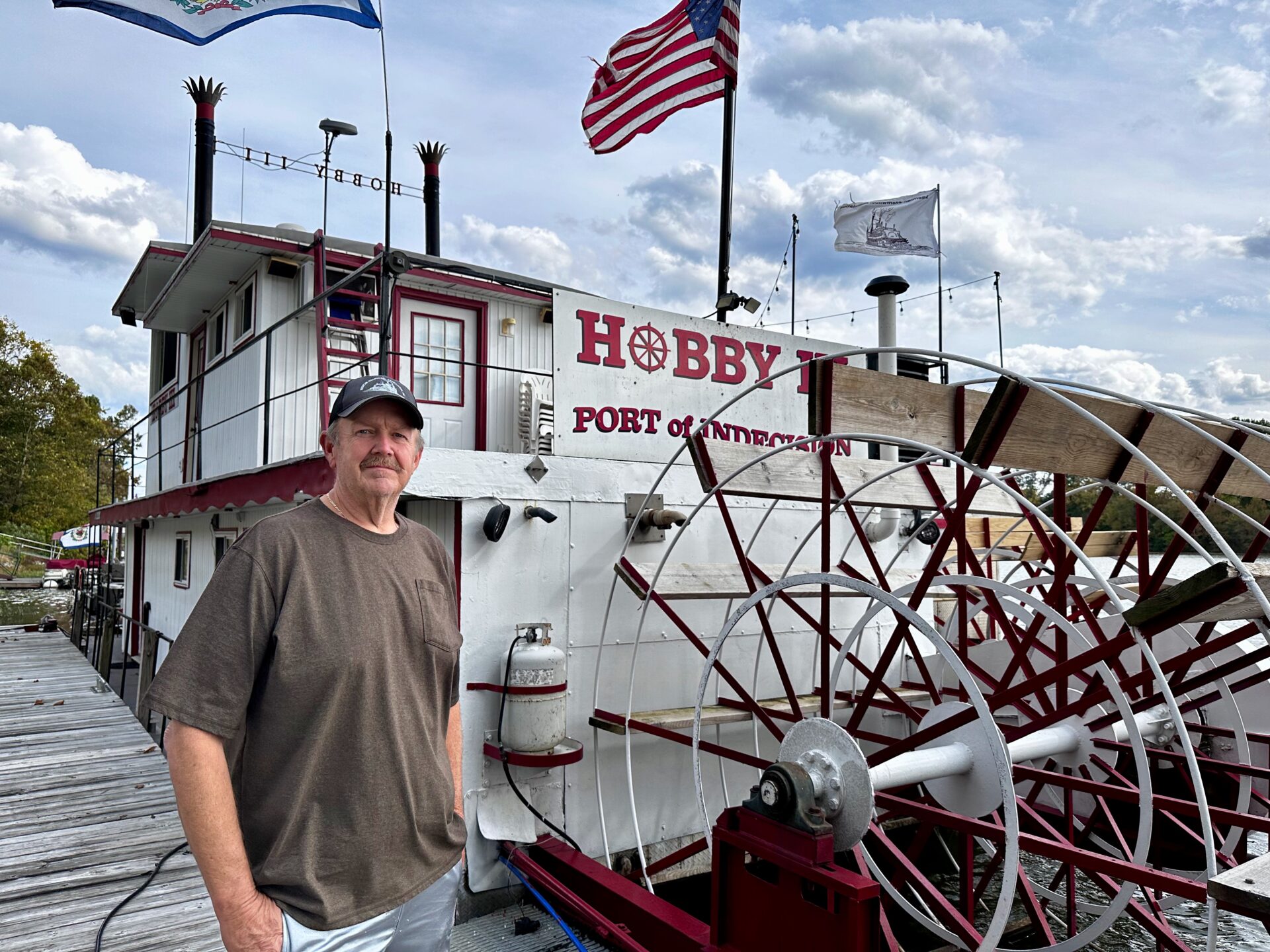 A man in a gray shirt stands in front of a sternwheeler.