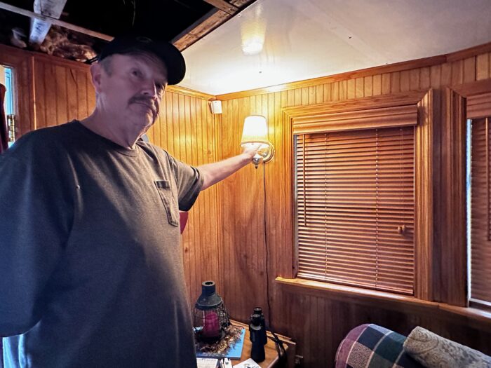 A man in a ball cap has his hand on the switch of a lamp on the wall of a boat.
