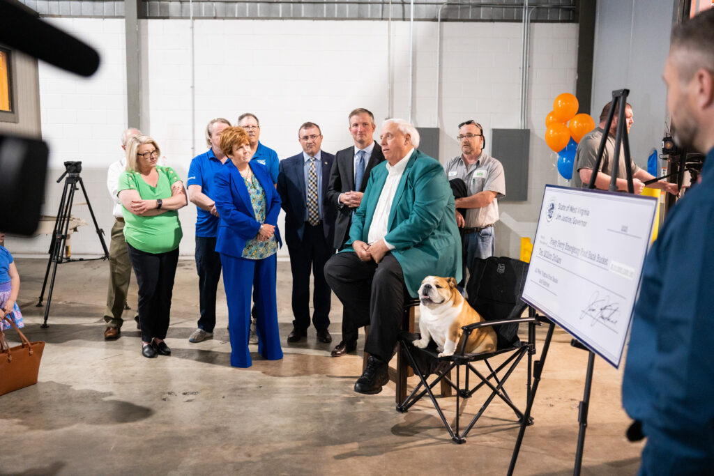 Big man with white hair and fat dog with people around him next to big check.