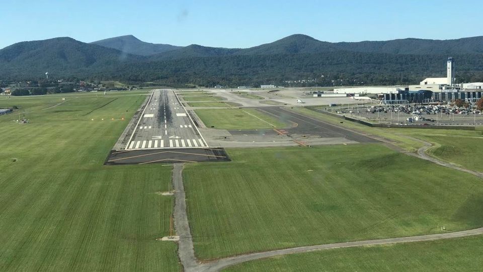 An overhead view of an airport runway with a mountain ridge in the background.