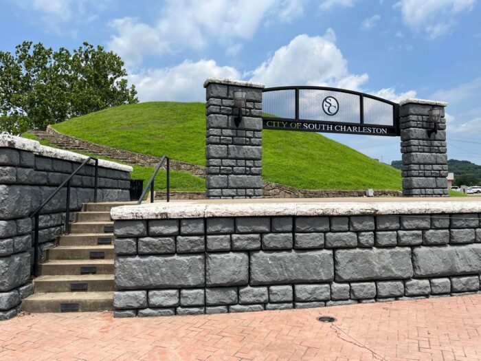 A grassy mound with a stone stairway and wall, with a large sign that identifies the location.