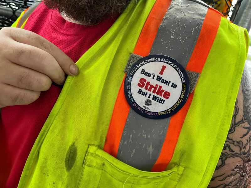 A worker wearing a yellow vest points to a white button that indicates he's on strike.