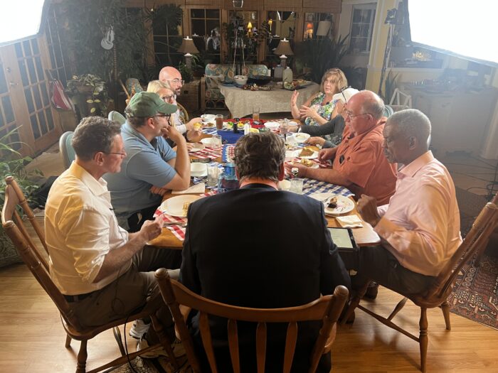 Nine adults sit around a dinner table. Six men and three women.