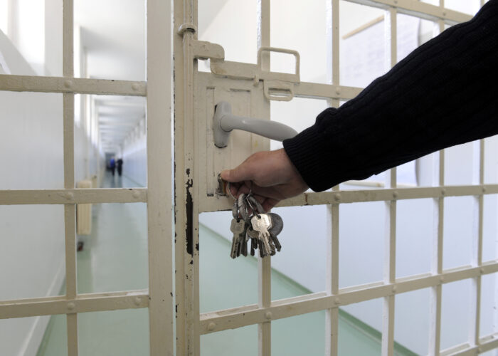 A correctional officer's arm is shown locking a jail door to an adjoining hallway. The officer is wearing a black long sleeve shirt.