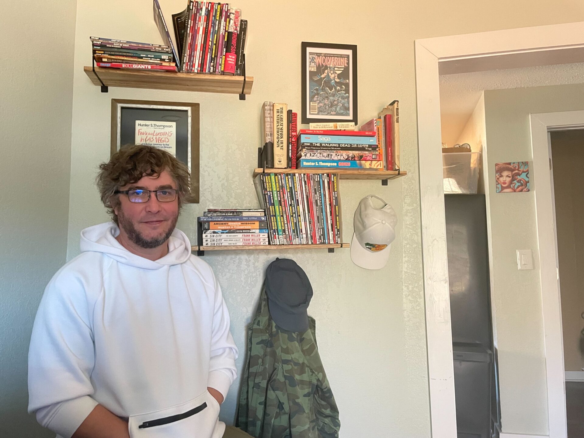 Man in white hoodie sits Infront of bookshelves.