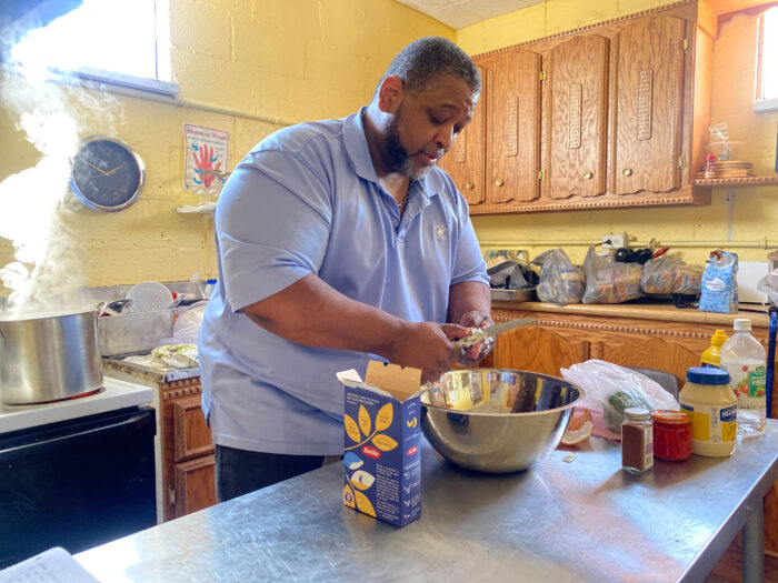 Large man in a blue polo cuts onions over a bowl in a kitchen.