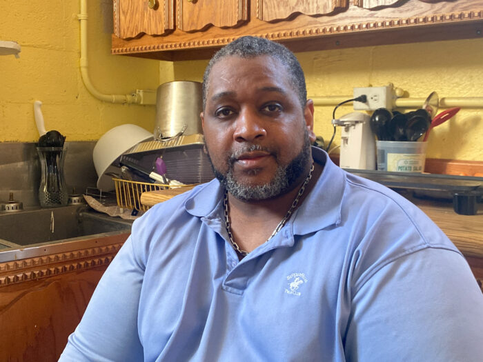 A large man in a blue polo poses for a photo in his kitchen.