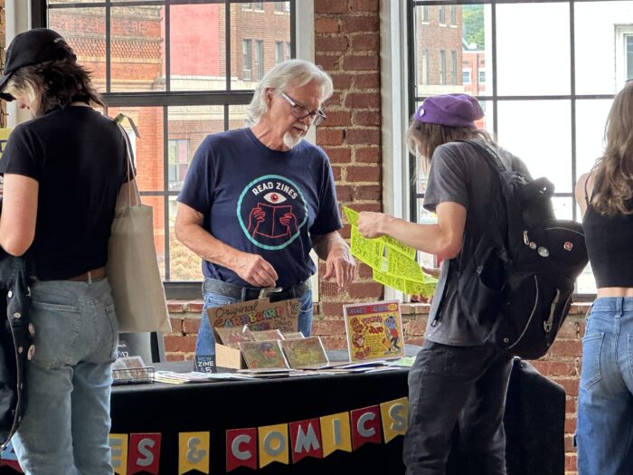 A zinemaker talks with a customer at a festival.