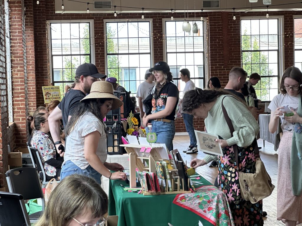 Dozens of people browse zines at a festival.