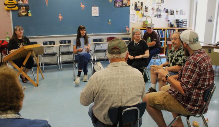 People sit around in a circle playing wooden spoons in a classroom.