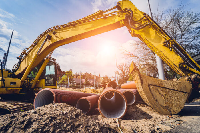 Heavy equipment and large pipes against a blue sky backdrop with the sun shining.