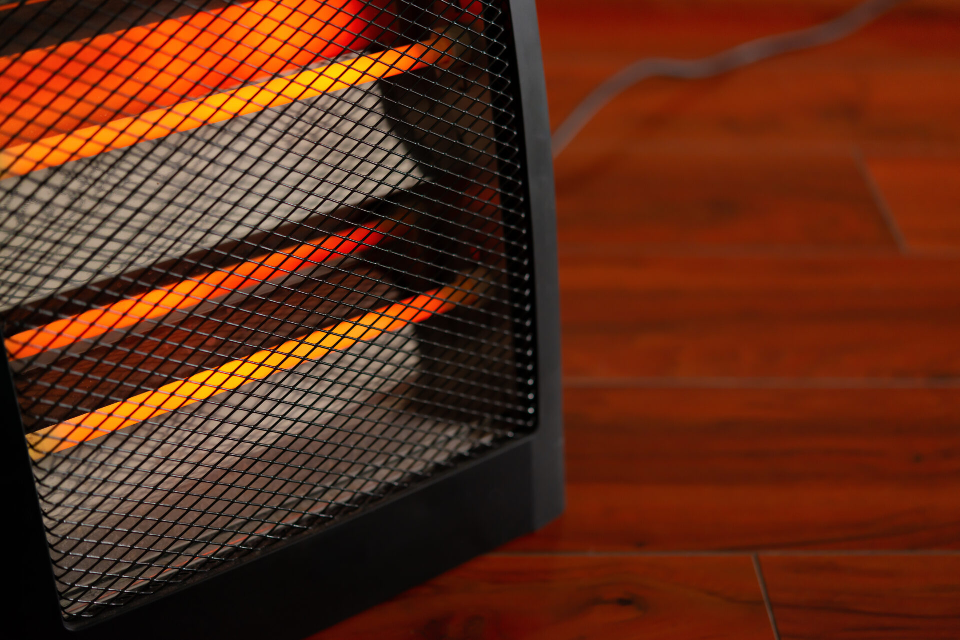 A close up of an electric heater is shown in a room with hardwood floors.