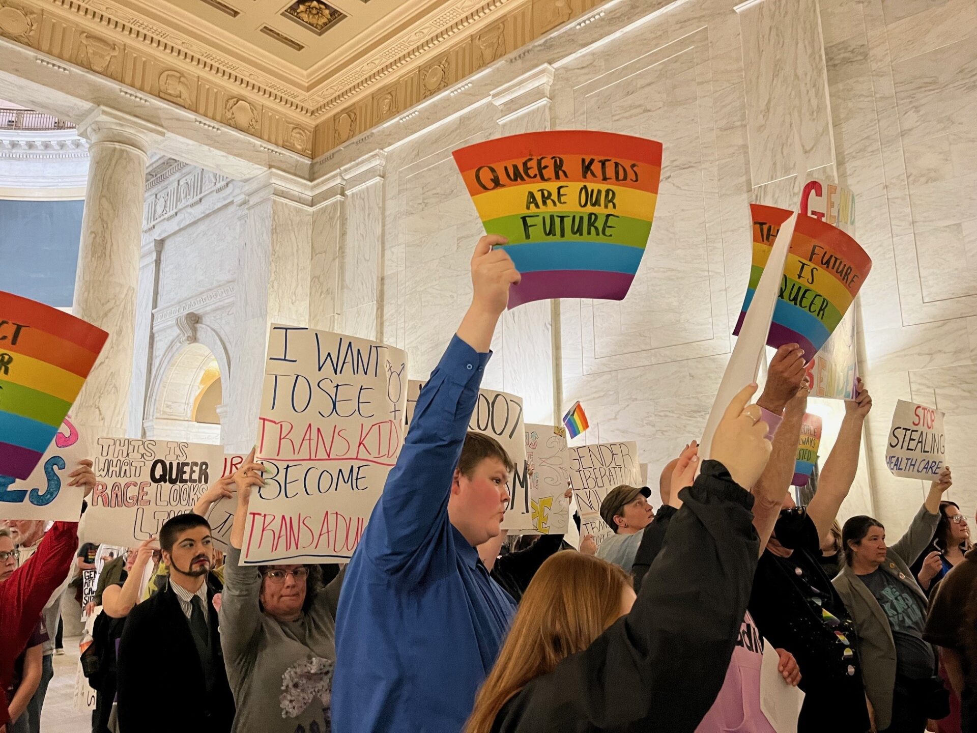 A group of protesters occupy a large space carrying colorful signs.