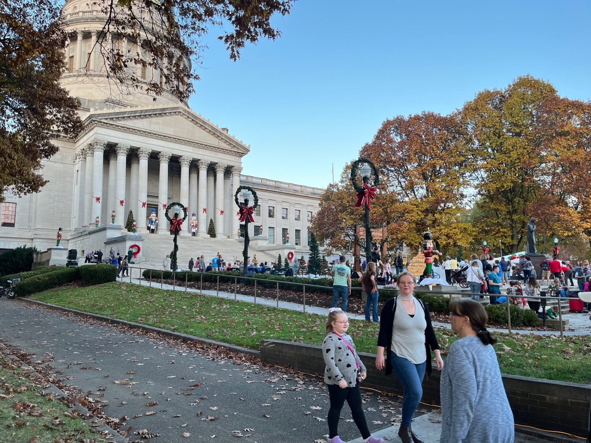 A stone building with large columns and a dome with people gathered in front and Christmas decorations in the foreground.