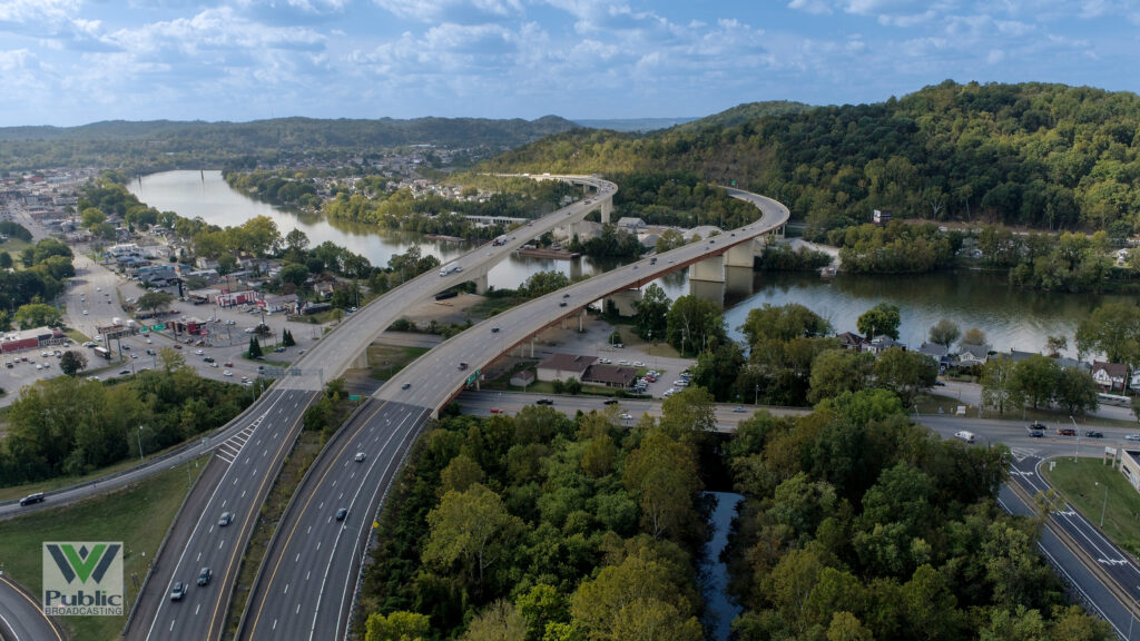 A multilane highway winds through a scene and crosses a river at the mouth of a creek under a partly cloudy sky.