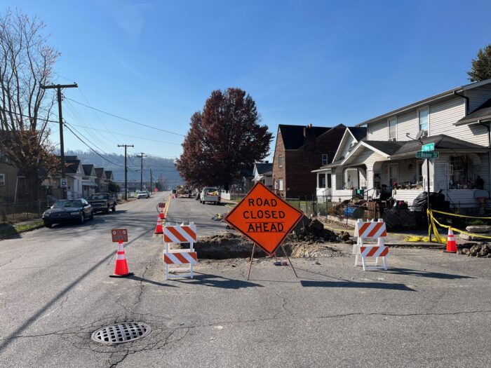 Mounds of dirt surround holes in the street with orange caution signs and cones to warn drivers.